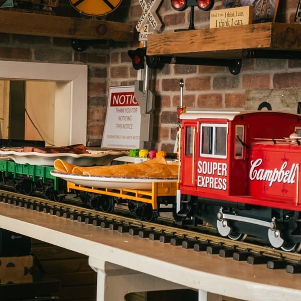 A red Campbell's "Souper Express" model train carries food on tracks through a brick-walled restaurant.