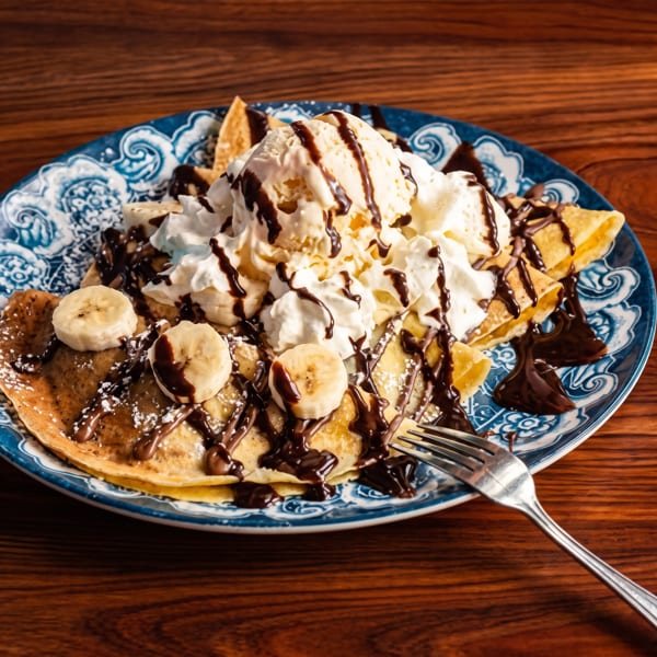 Banana crepes with vanilla ice cream, whipped cream, chocolate syrup, and powdered sugar.