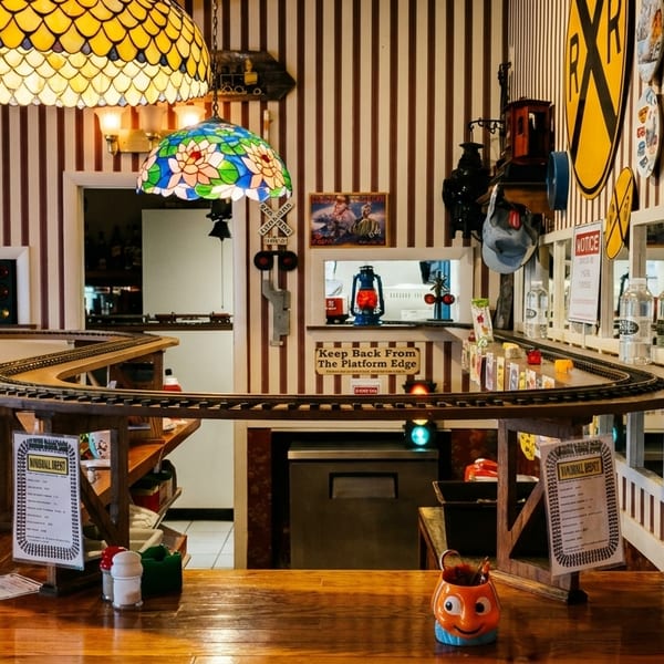 Restaurant interior with train tracks on a counter, striped walls, and stained-glass lamps.