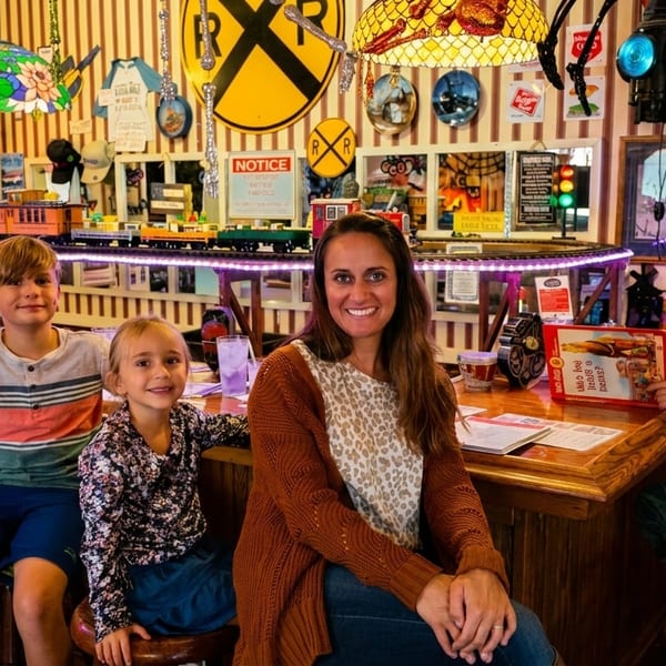A family of five, including a mother and four children, smiling at a restaurant bar with a toy train.