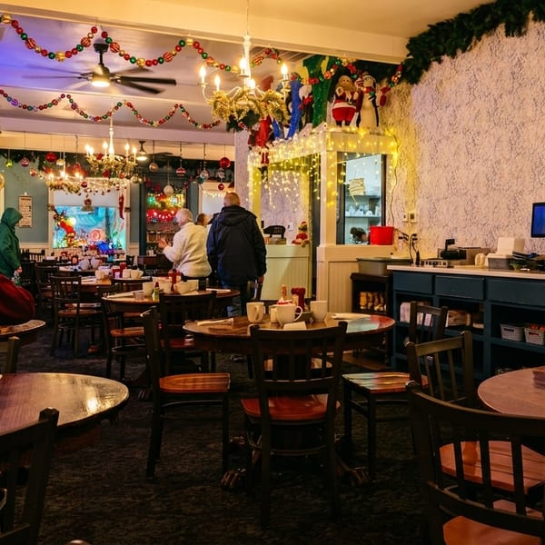 A cozy restaurant dining room decorated for Christmas, with patrons seated at wooden tables.