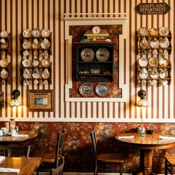 Cozy restaurant interior with striped and floral wallpaper, wooden tables, and decorative plates on walls.