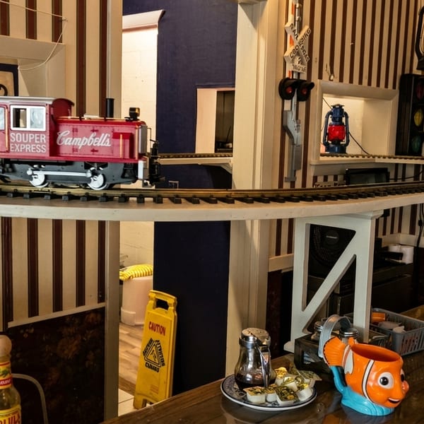 A model train carrying drinks on an elevated track above a restaurant counter with striped walls.