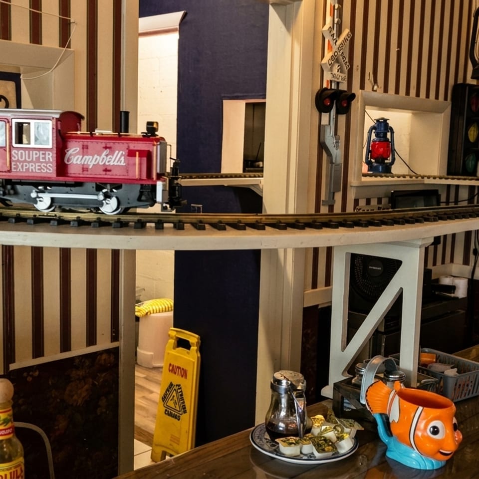 A model train carrying drinks on an elevated track above a restaurant counter with striped walls.